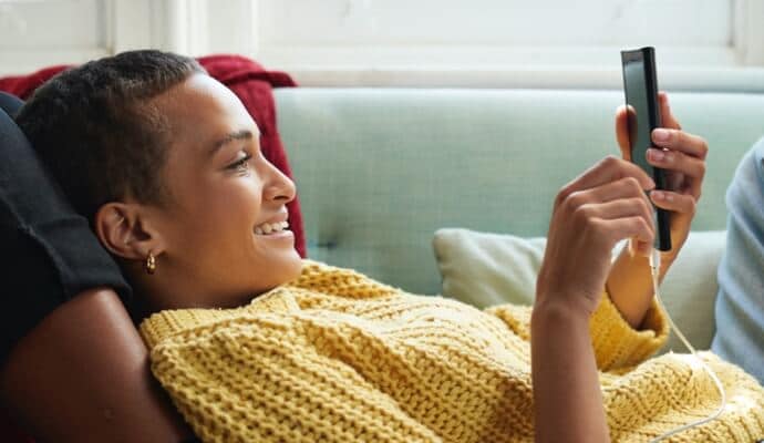 女性在沙發上看著手機，畫面上是 AntiVirus Plus 正在啟動 Norton 360。