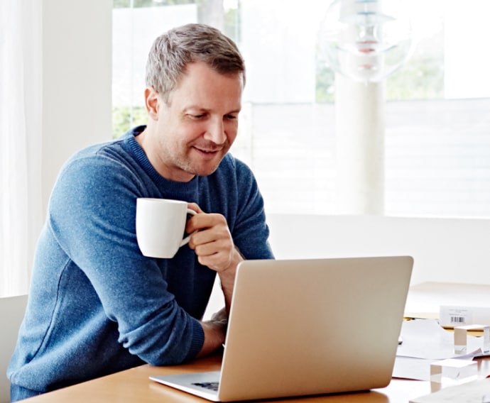 在家一邊使用筆記型電腦一邊喝咖啡的男人。